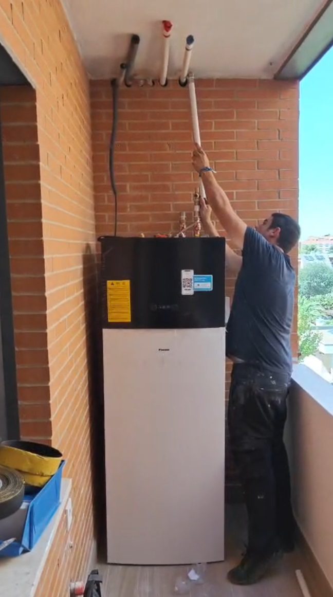 Instalador conectando las tuberías de la unidad de aerotermia en una vivienda de Madrid